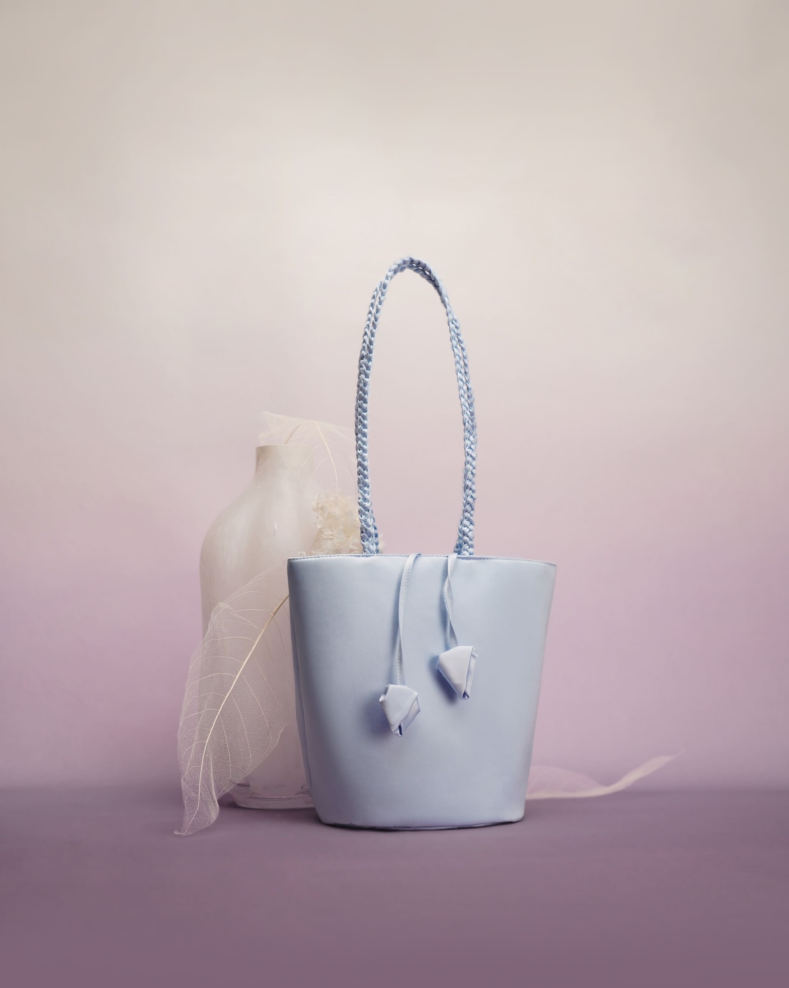 Sky blue satin bucket bag with braided strap on lilac backdrop