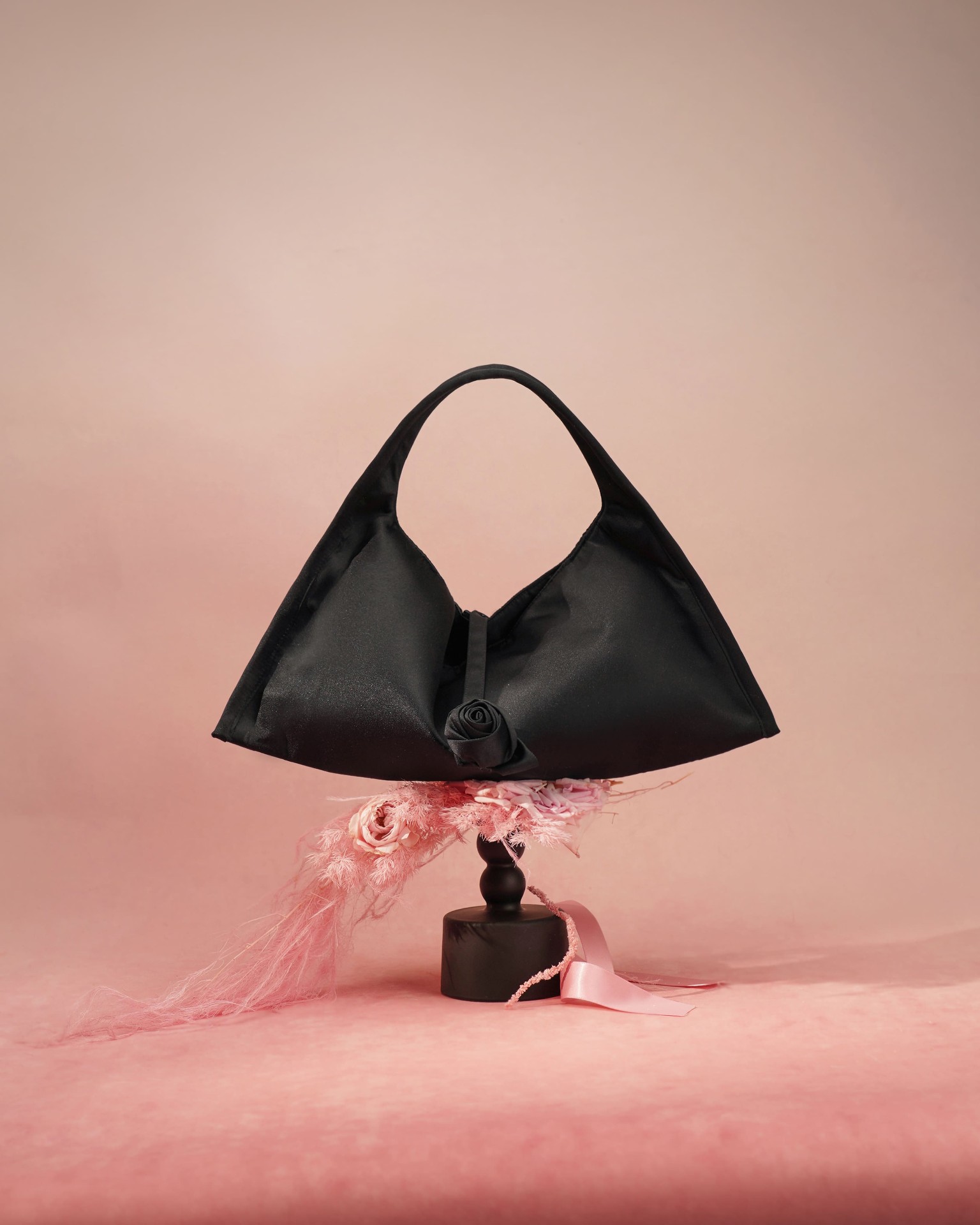 Black satin shoulder bag with rose detail on pink backdrop