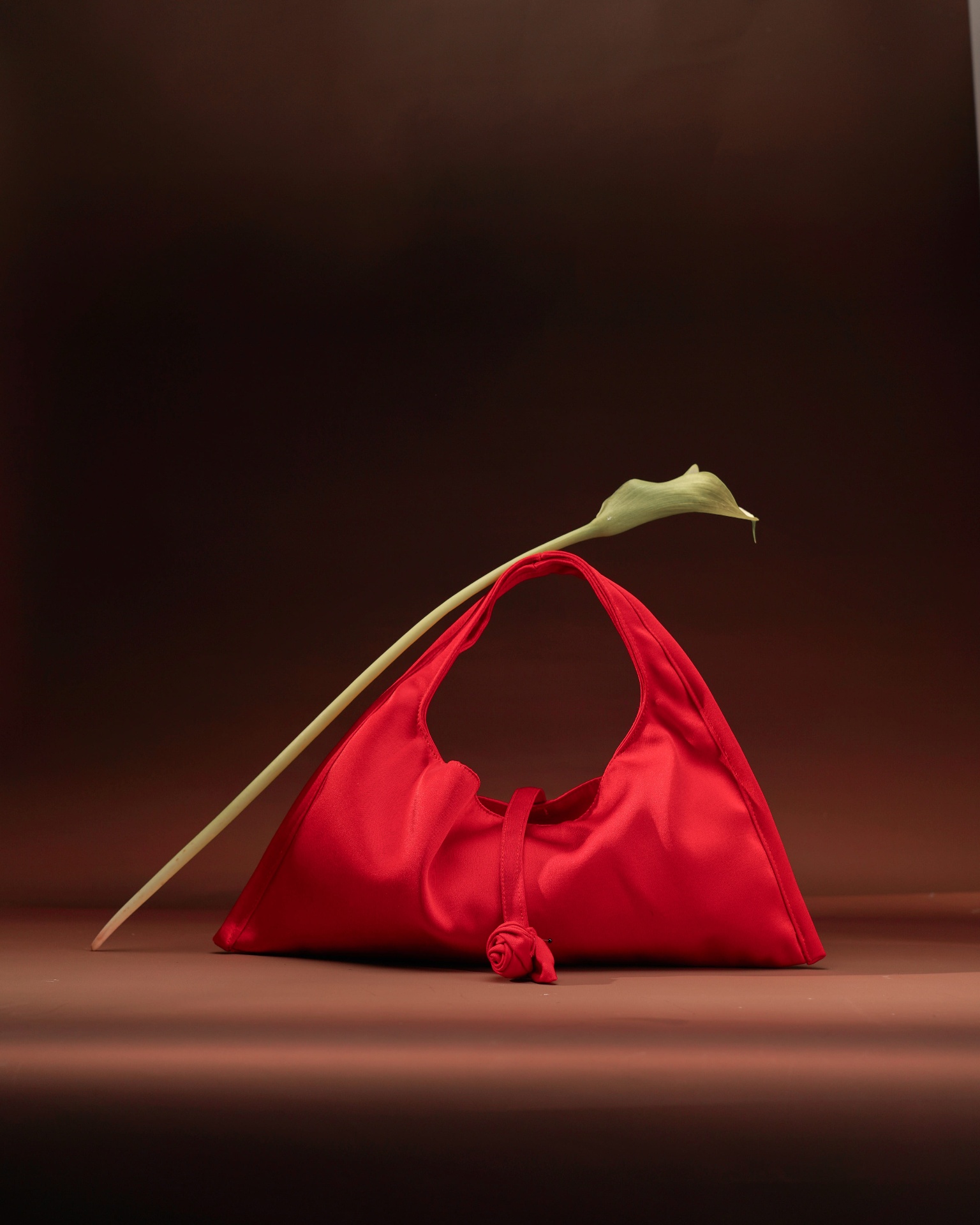 Red satin shoulder bag with calla lily on burgundy backdrop